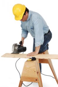 carpenter wearing a hard hat and demins about to cut a plank with a power saw