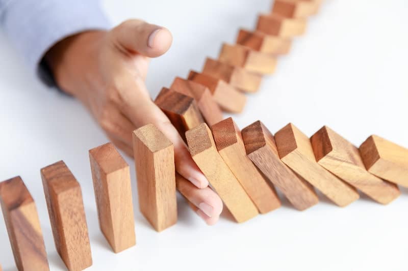 A man's hand prevents a row of falling dominos from knocking down more of them.
